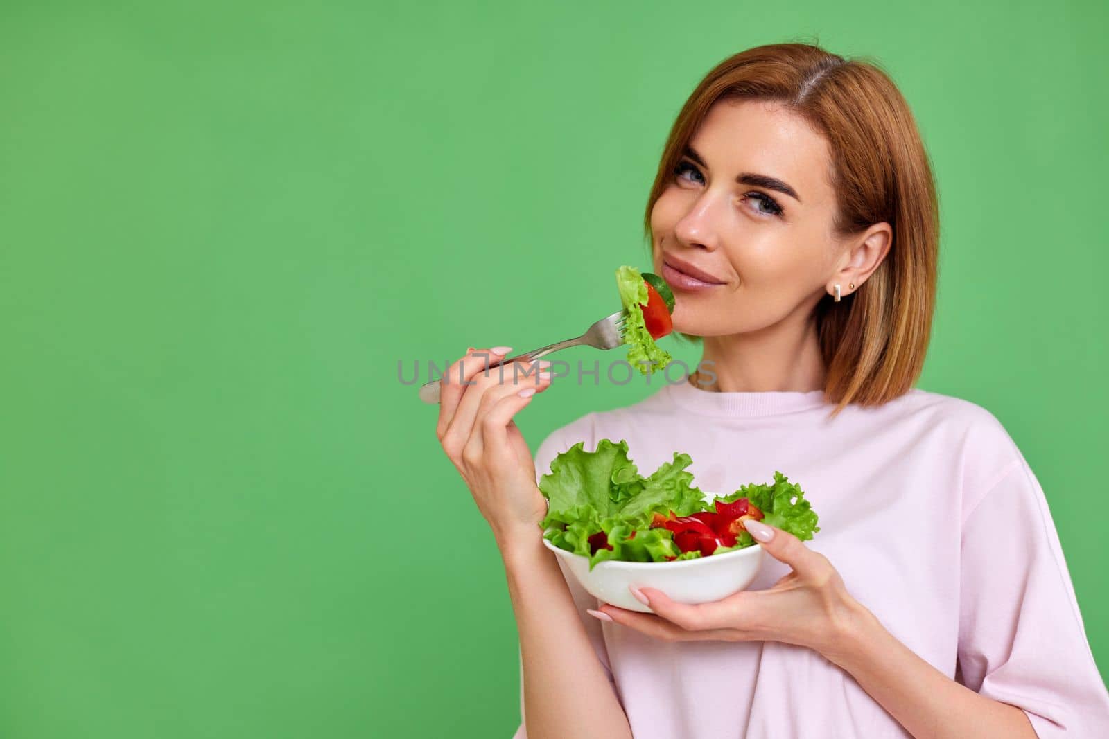 beautiful healthy woman eating fresh vegetable salad on green background. copy space