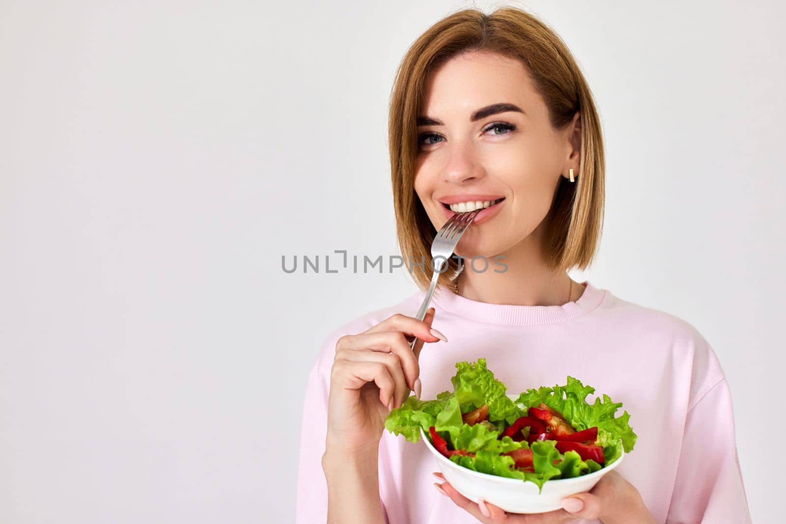 smiling healthy blonde woman eating fresh vegetable salad on white background. copy space