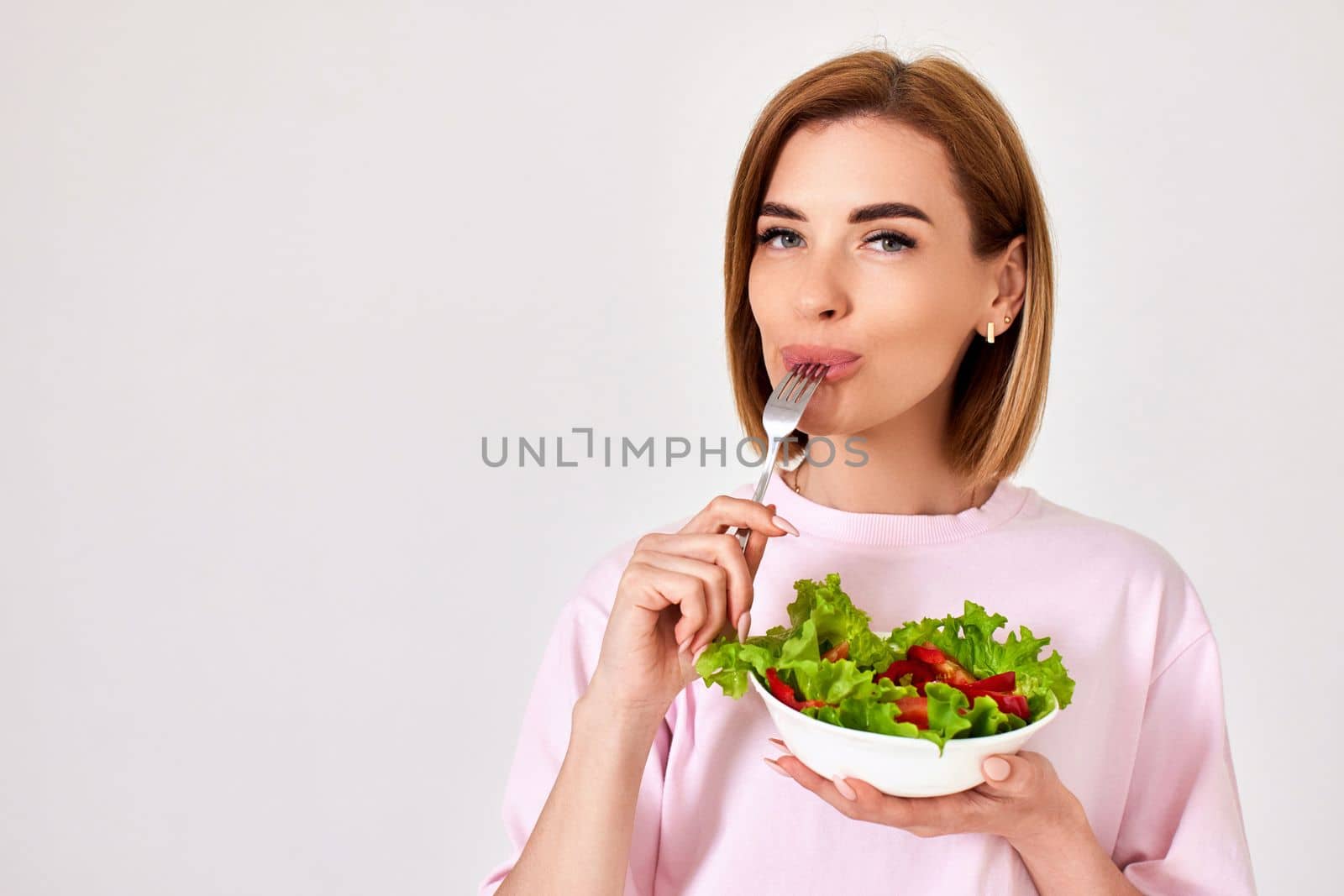 attractive caucasian woman eating fresh vegetable salad on white background