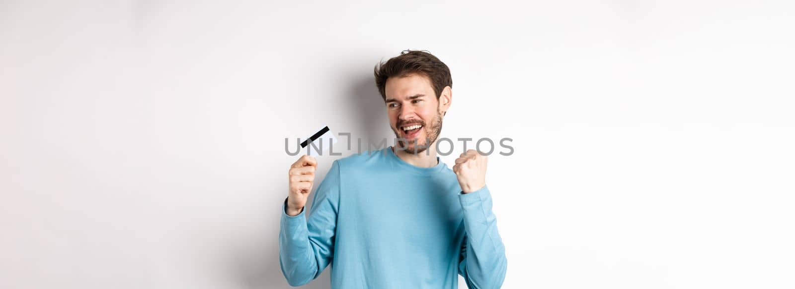 Happy man dancing with plastic credit card, smiling and saying yes, celebrating on white background by Benzoix