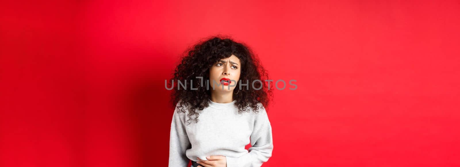 Woman feeling sick, bending and touching belly, having stomach ache or menstrual cramps, standing on red background.