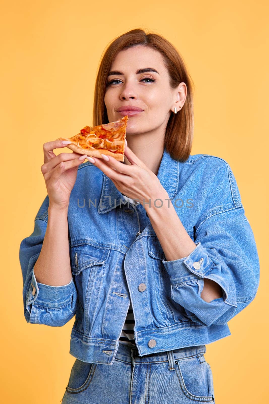 beautiful young woman holding with pleasure pizza slice on yellow background.