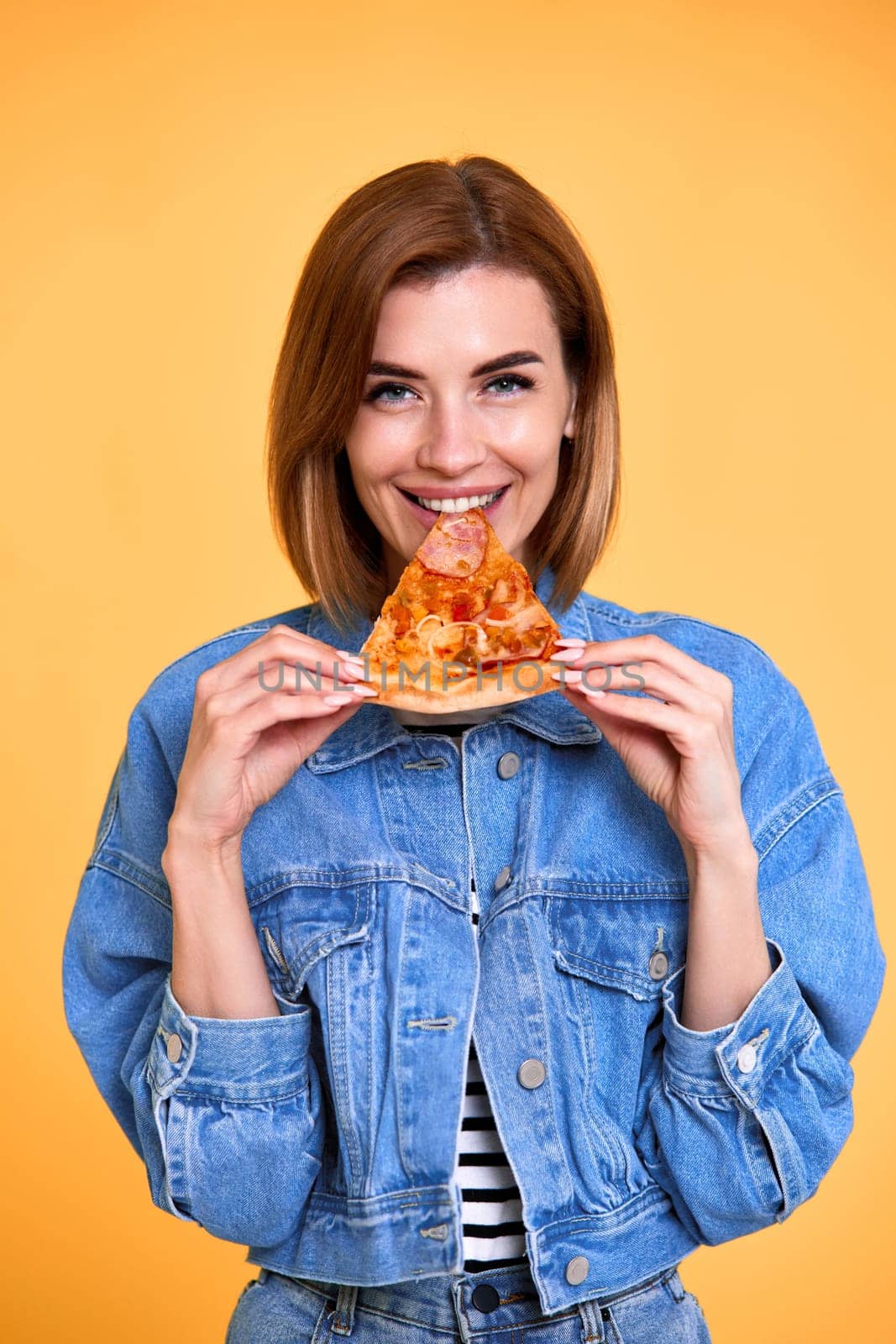 happy woman biting pizza slice on yellow background