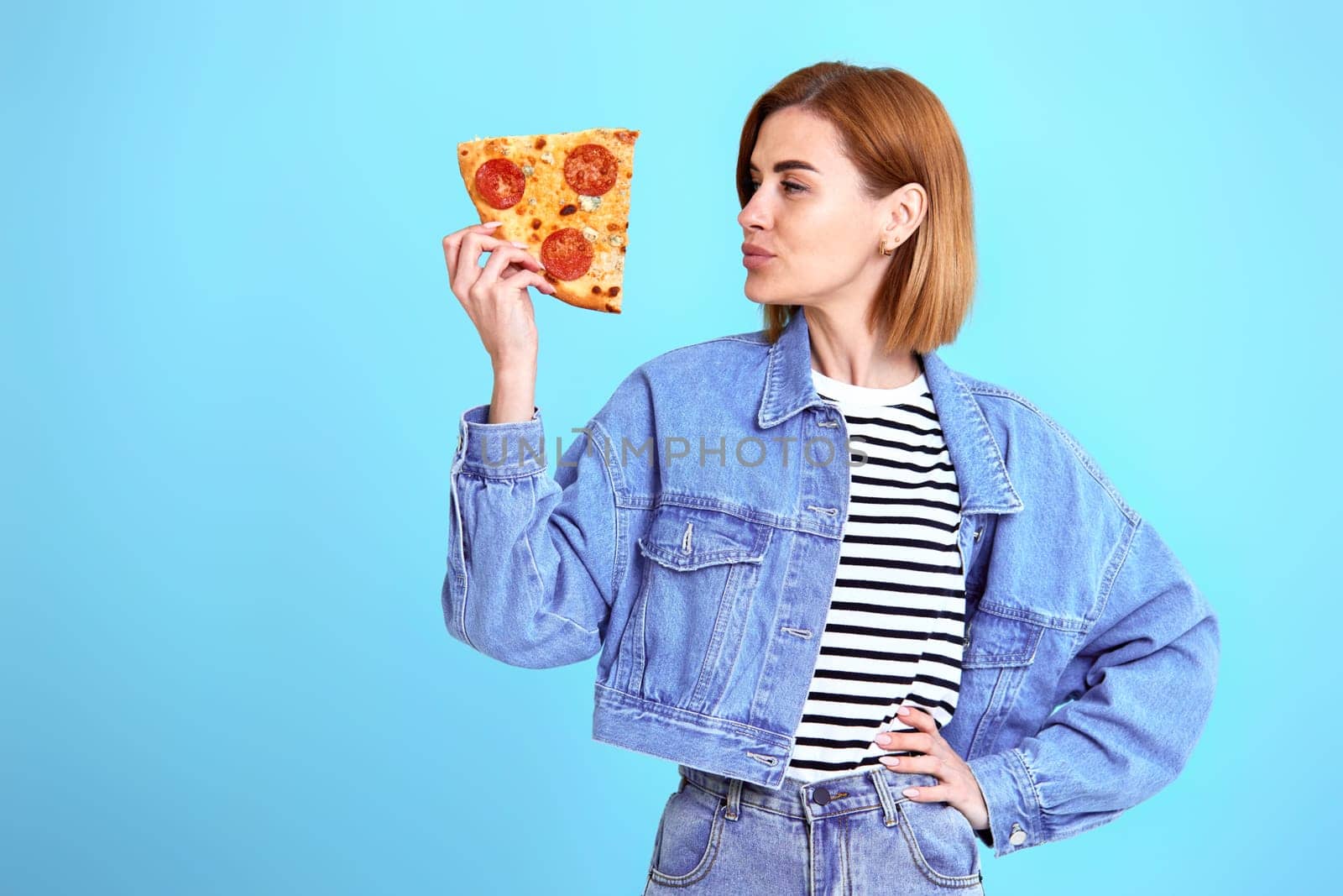 beautiful young woman with pizza slice on blue background. copy space