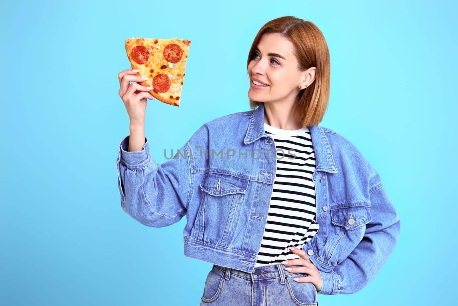 beautiful young woman with pizza slice on blue background. copy space