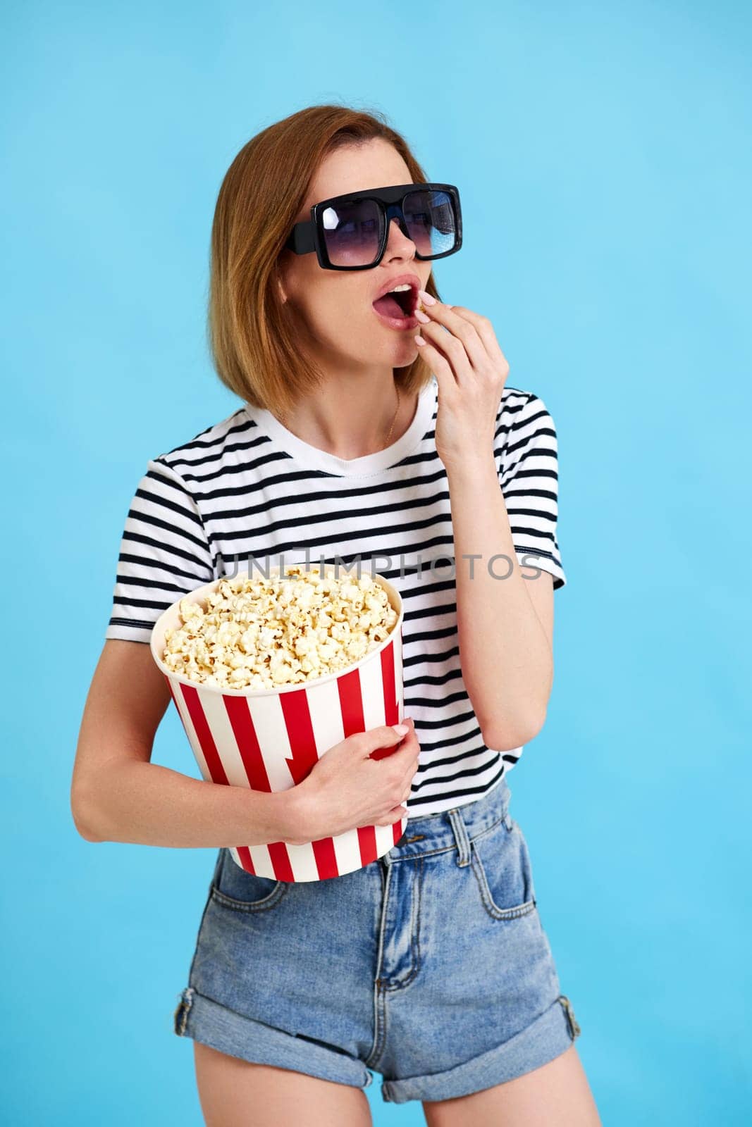 woman watching movie film, holding bucket of popcorn isolated on blue background