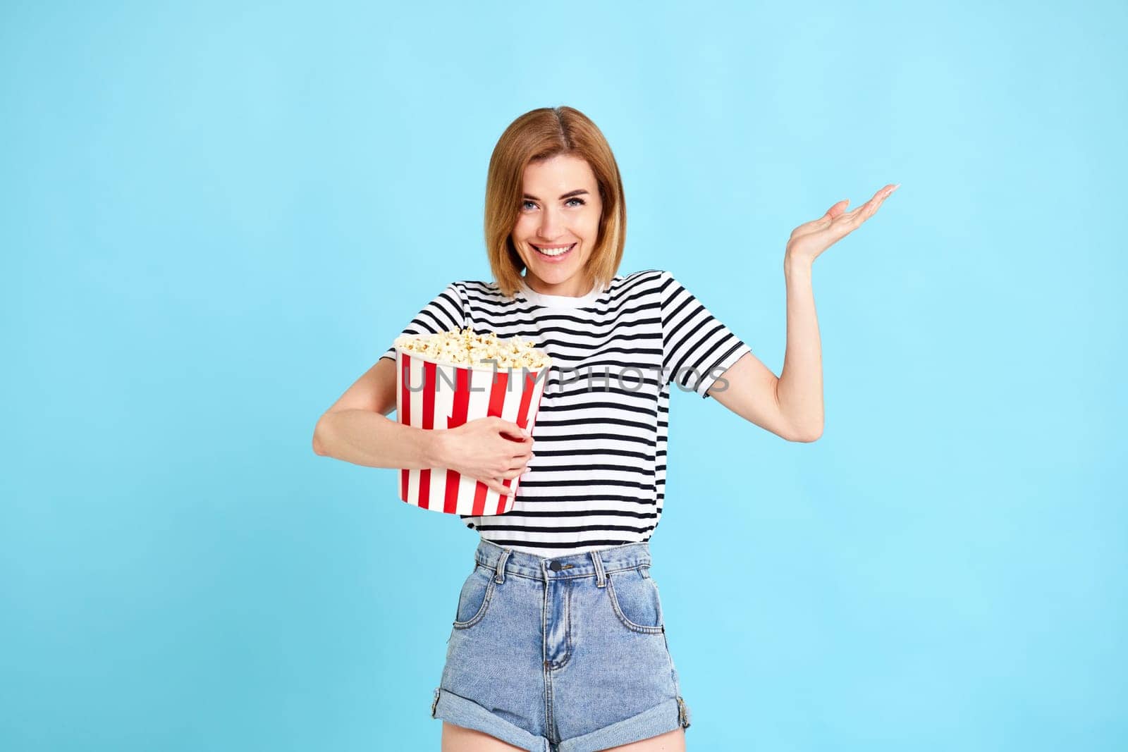 woman watching movie film, holding bucket of popcorn isolated on blue background