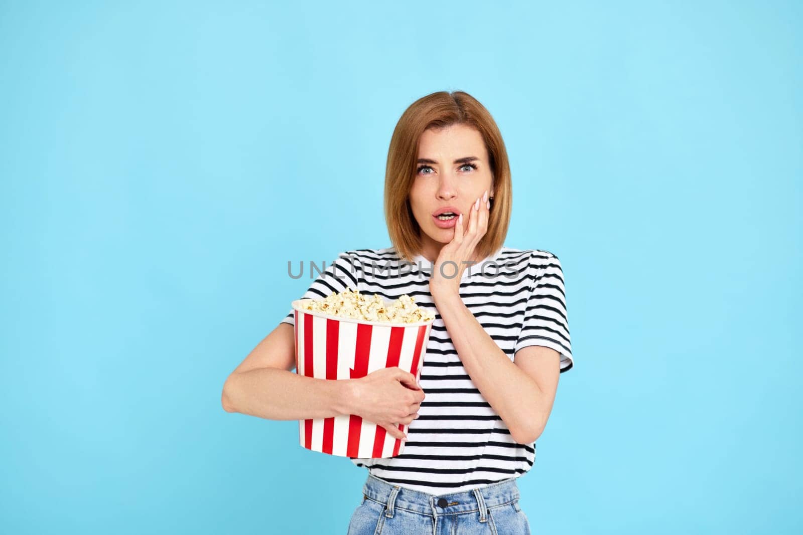 feared frightened woman watching movie film, holding bucket of popcorn isolated on blue background