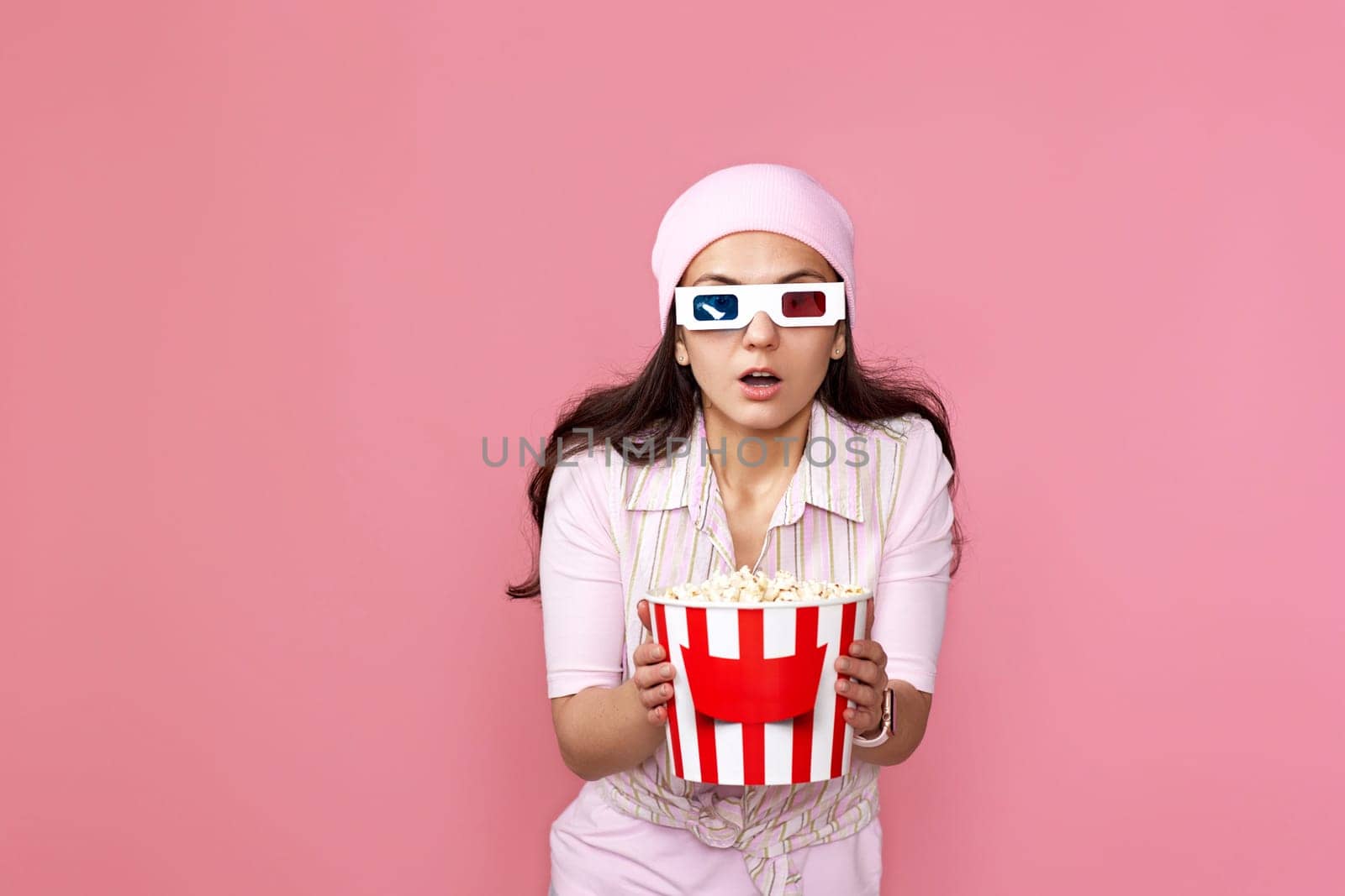 scared terrified woman watching movie film, holding bucket of popcorn on pink background