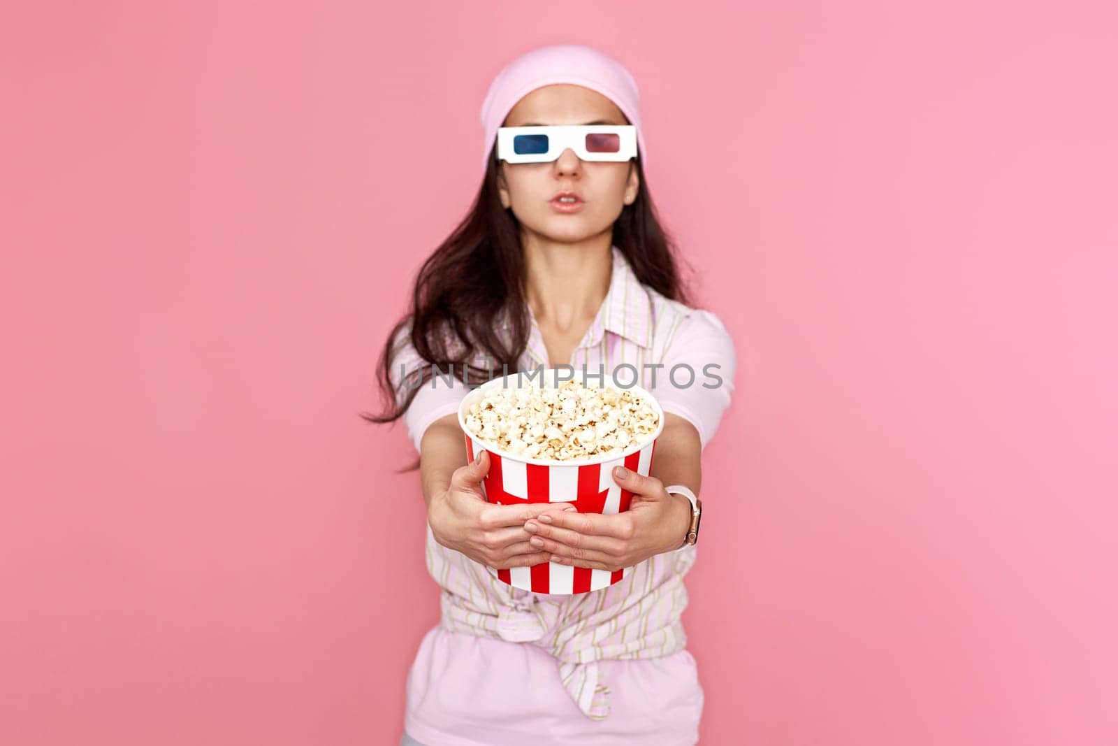 pretty woman holding bucket of popcorn isolated on pink background. focus on popcorn