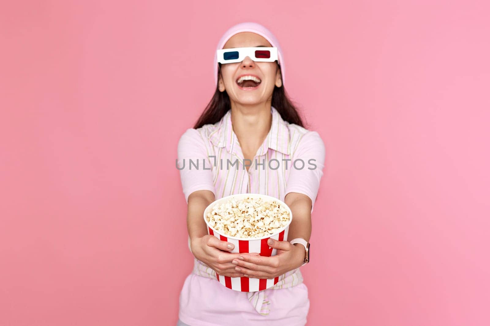 laughing woman watching comedy holding bucket of popcorn isolated on pink background. focus on popcorn