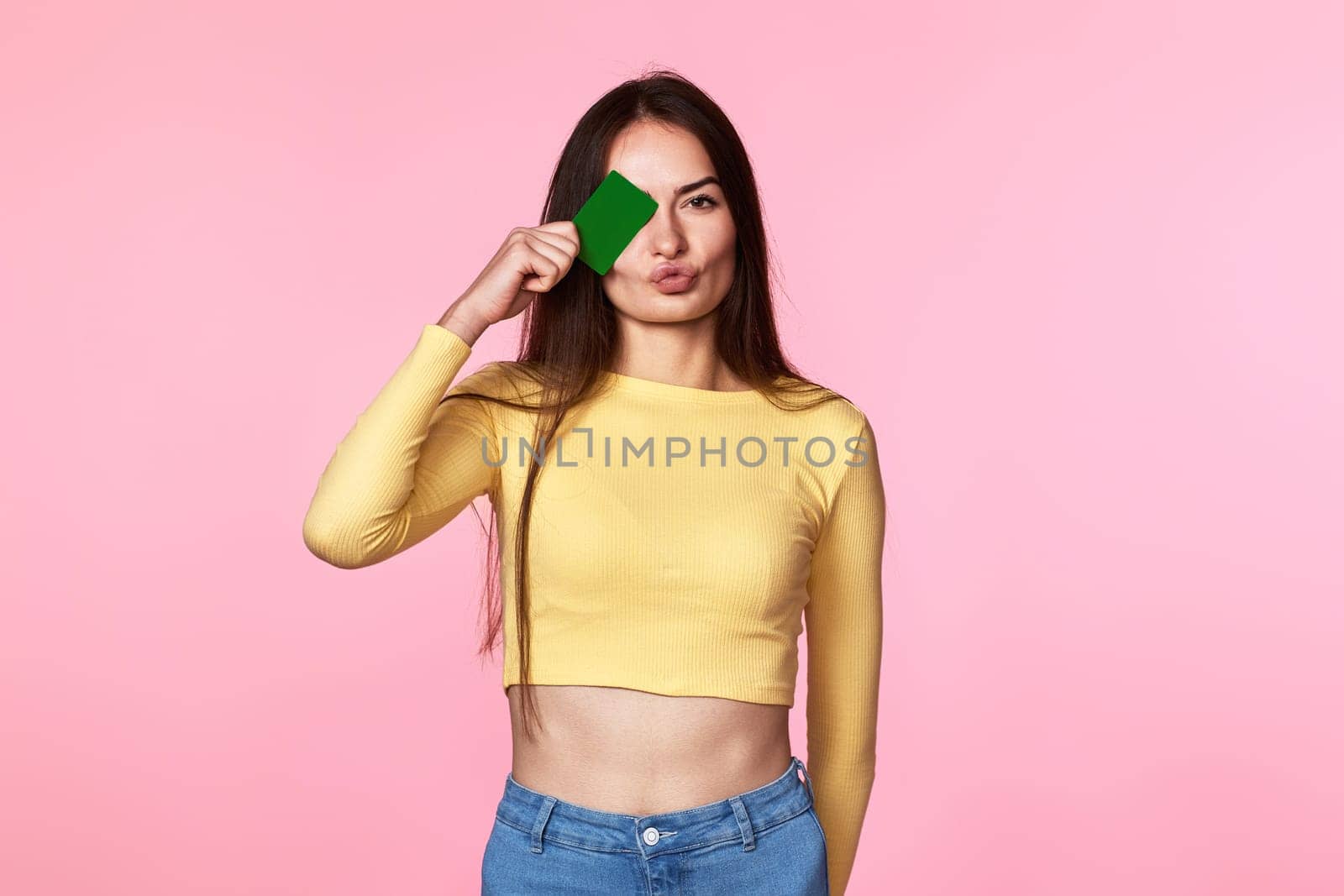 young woman covering eye with plastic credit card isolated on pink background