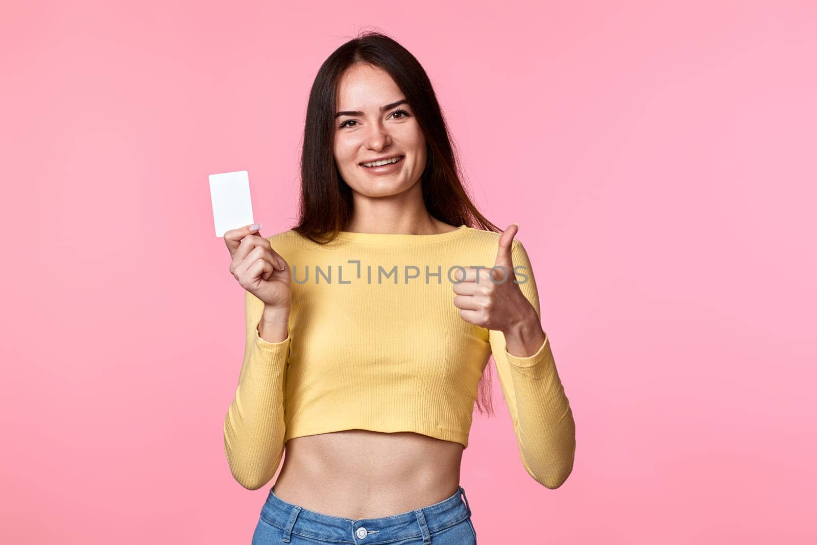 young woman in yellow clothes holding plastic credit card isolated on pink background