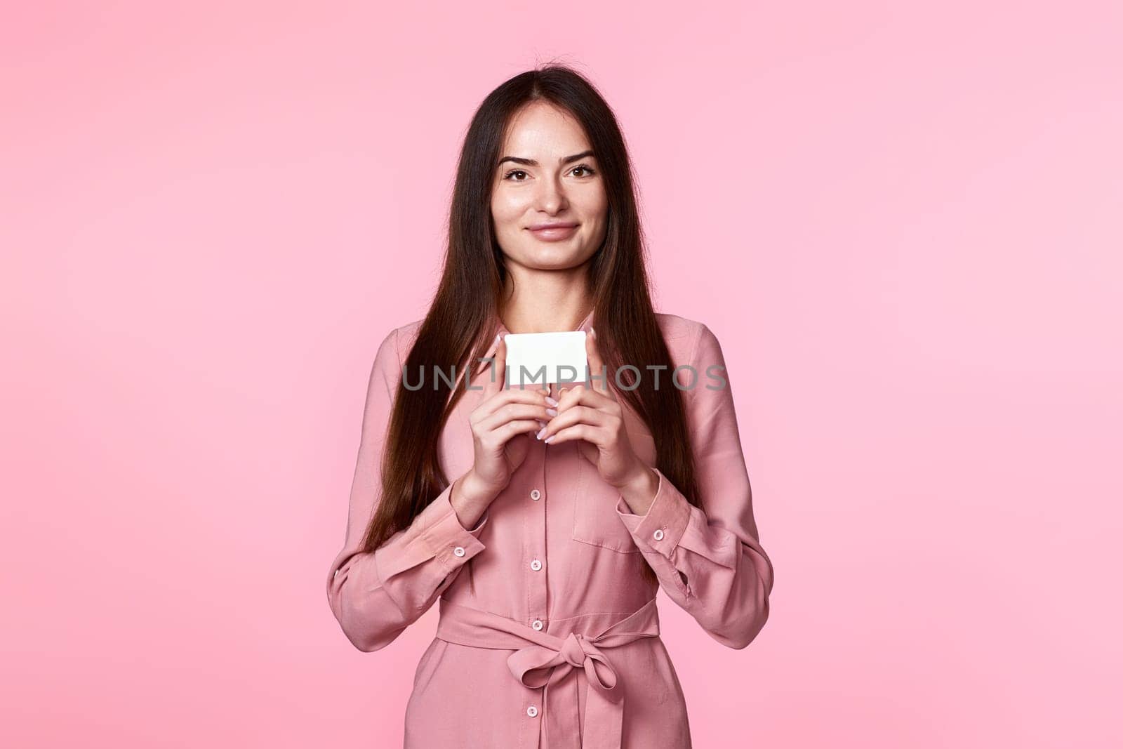young woman in pink dress holding plastic credit card isolated on pink background