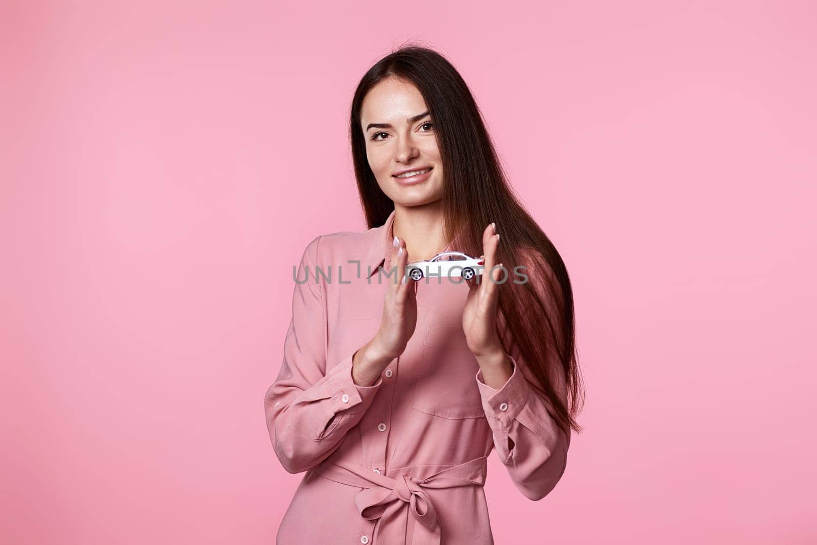beautiful woman in dress holding little white car on pink background. car protective and insurance