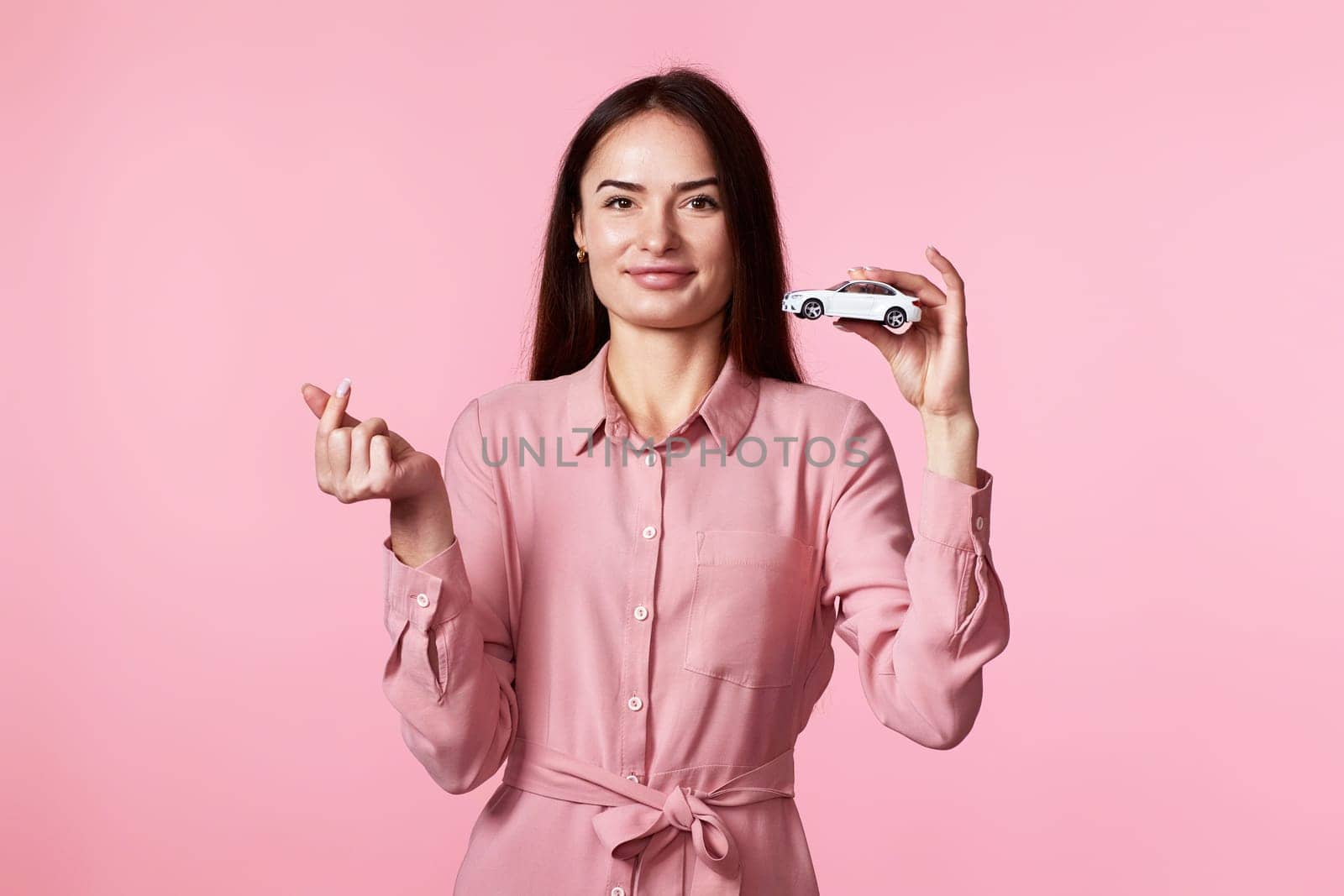 beautiful woman in dress holding little white car on pink background. car protective and insurance