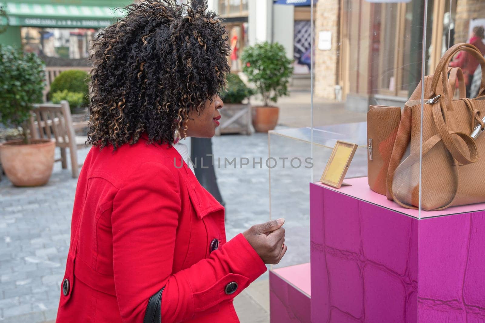 Happy confident curvy african american woman walks along a shopping street and looks at stylish bags in a shop window, High quality photo