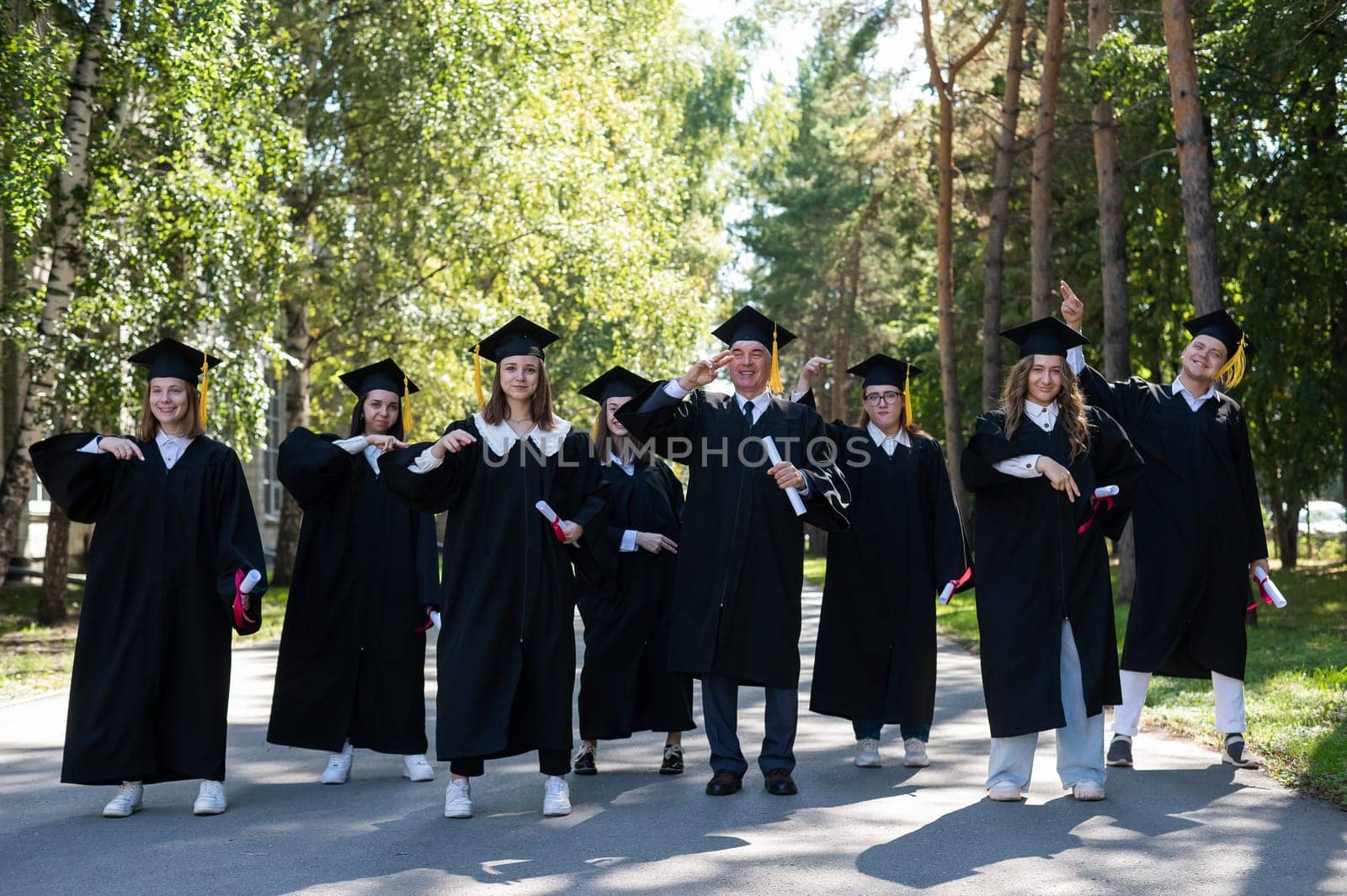 Group of graduates in robes dancing outdoors. Elderly student