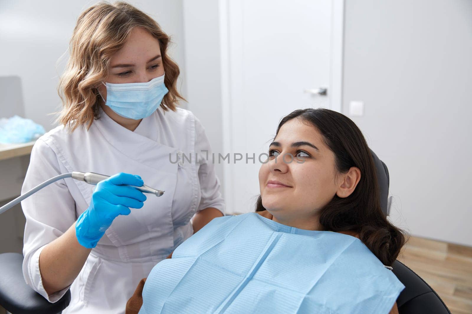 Dentist drilling tooth of female patient in dental chair by Mariakray