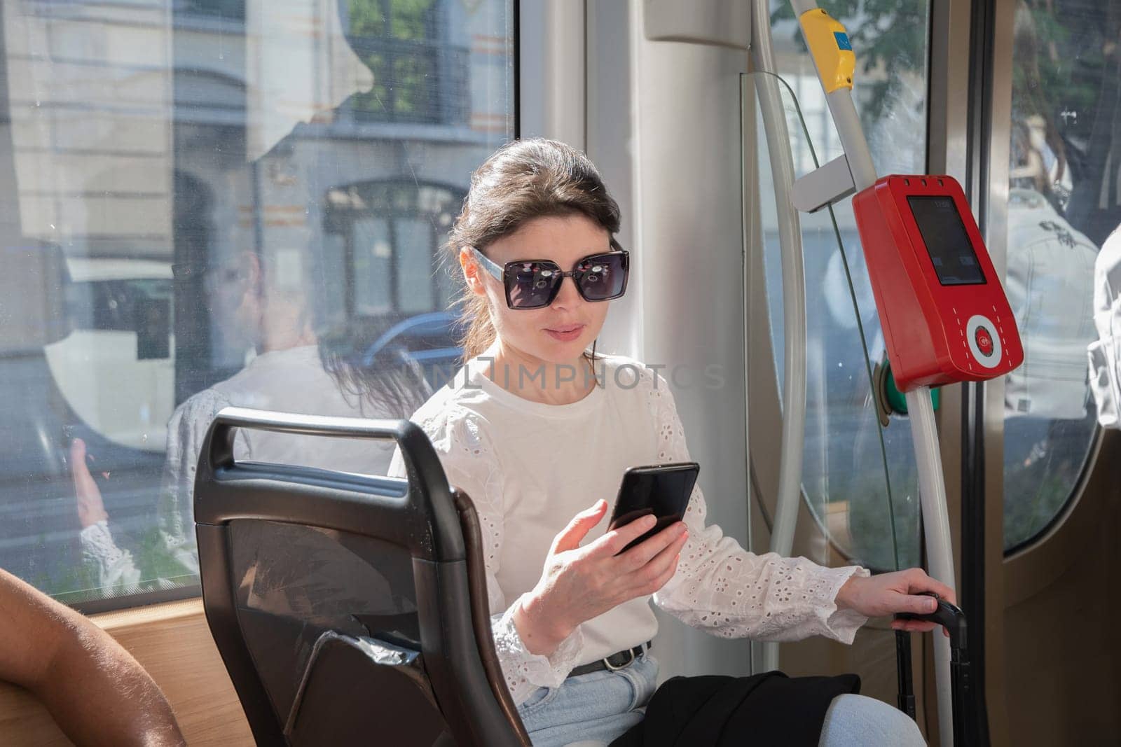 Young brunette browsing and typing messages on phone on way to work in tram, High quality photo