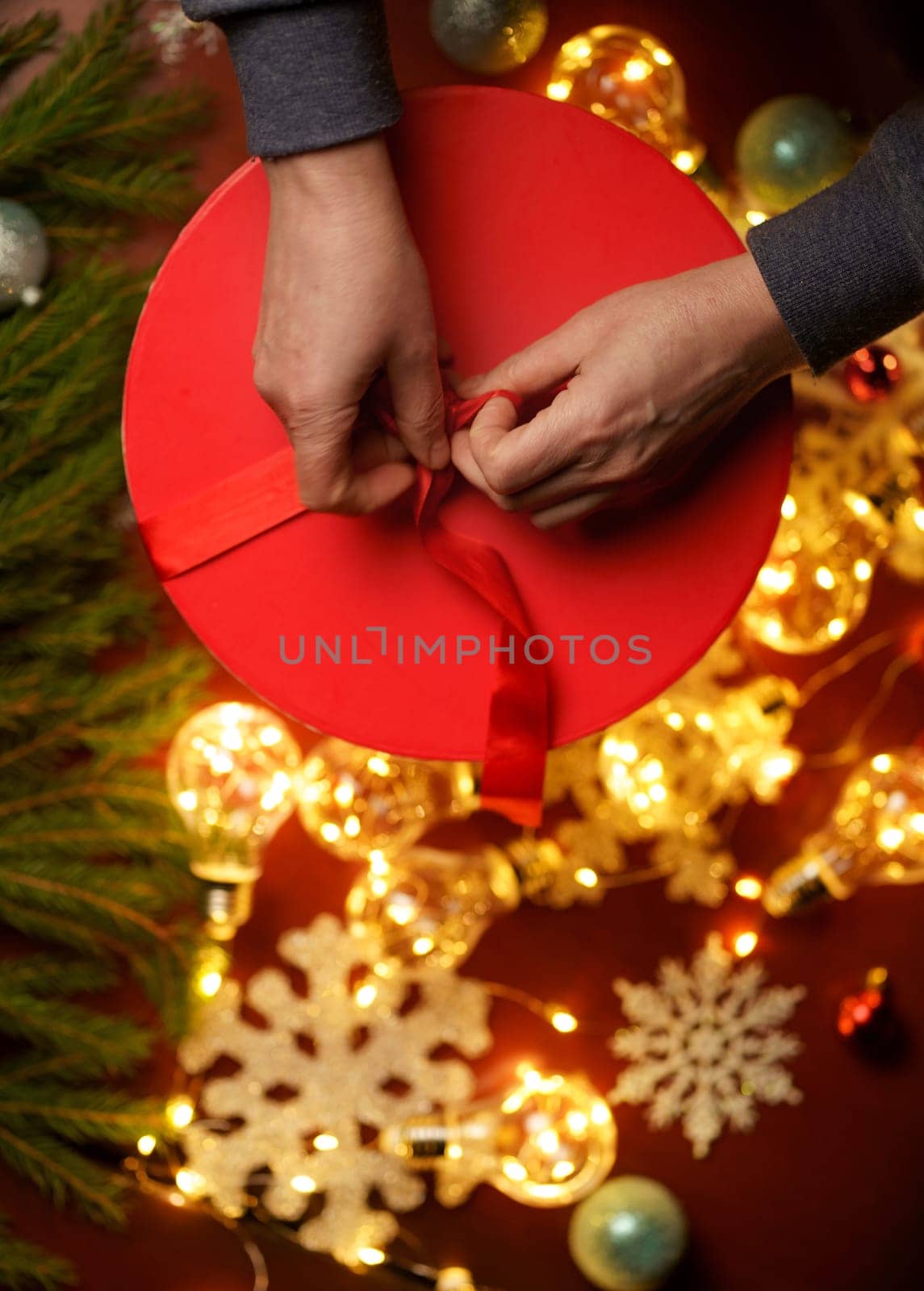 surrounded by Christmas toys on red gift box Hands tying ribbon