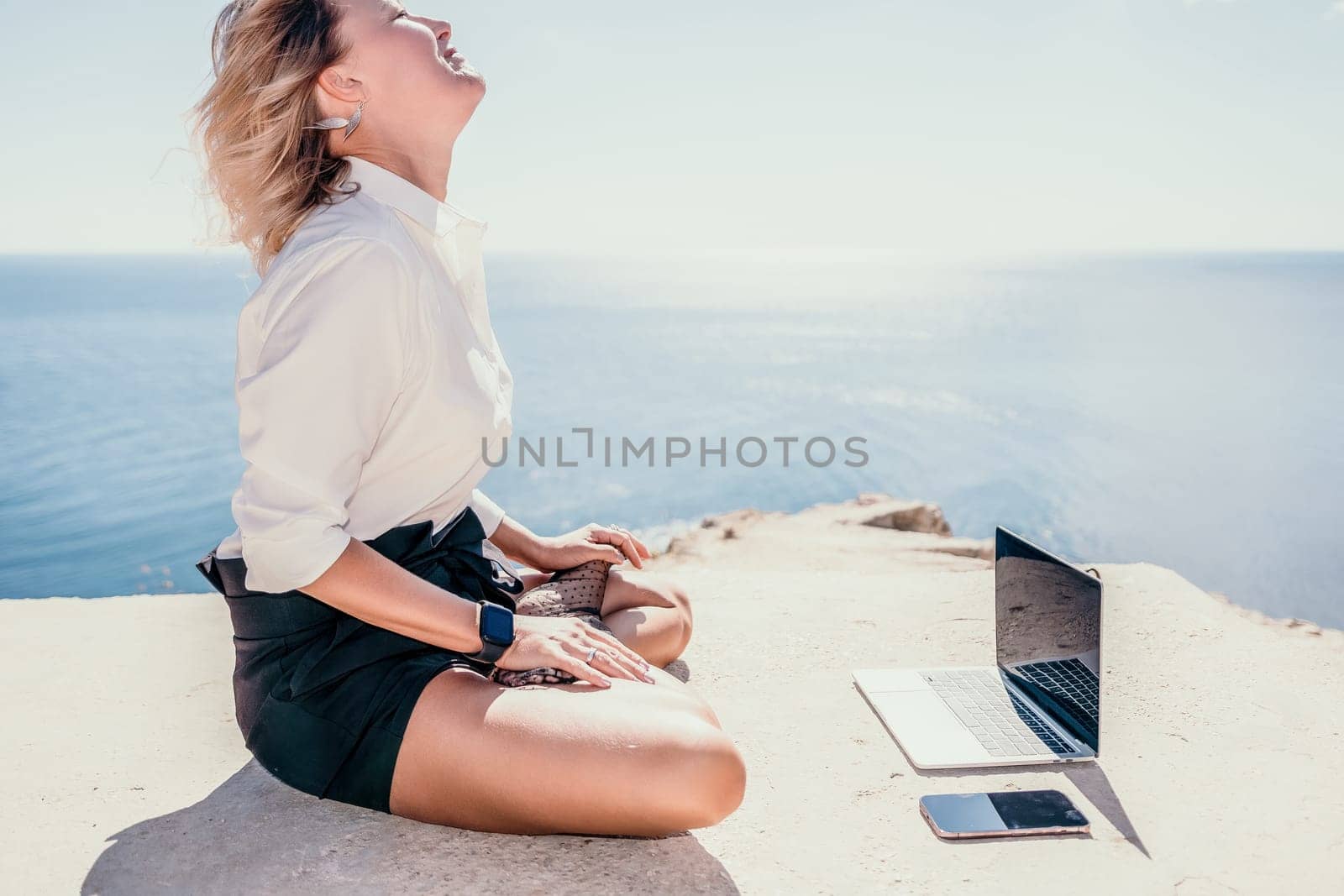 Happy girl doing yoga with laptop working at the beach. beautiful and calm business woman sitting with a laptop in a summer cafe in the lotus position meditating and relaxing. freelance girl remote work beach paradise