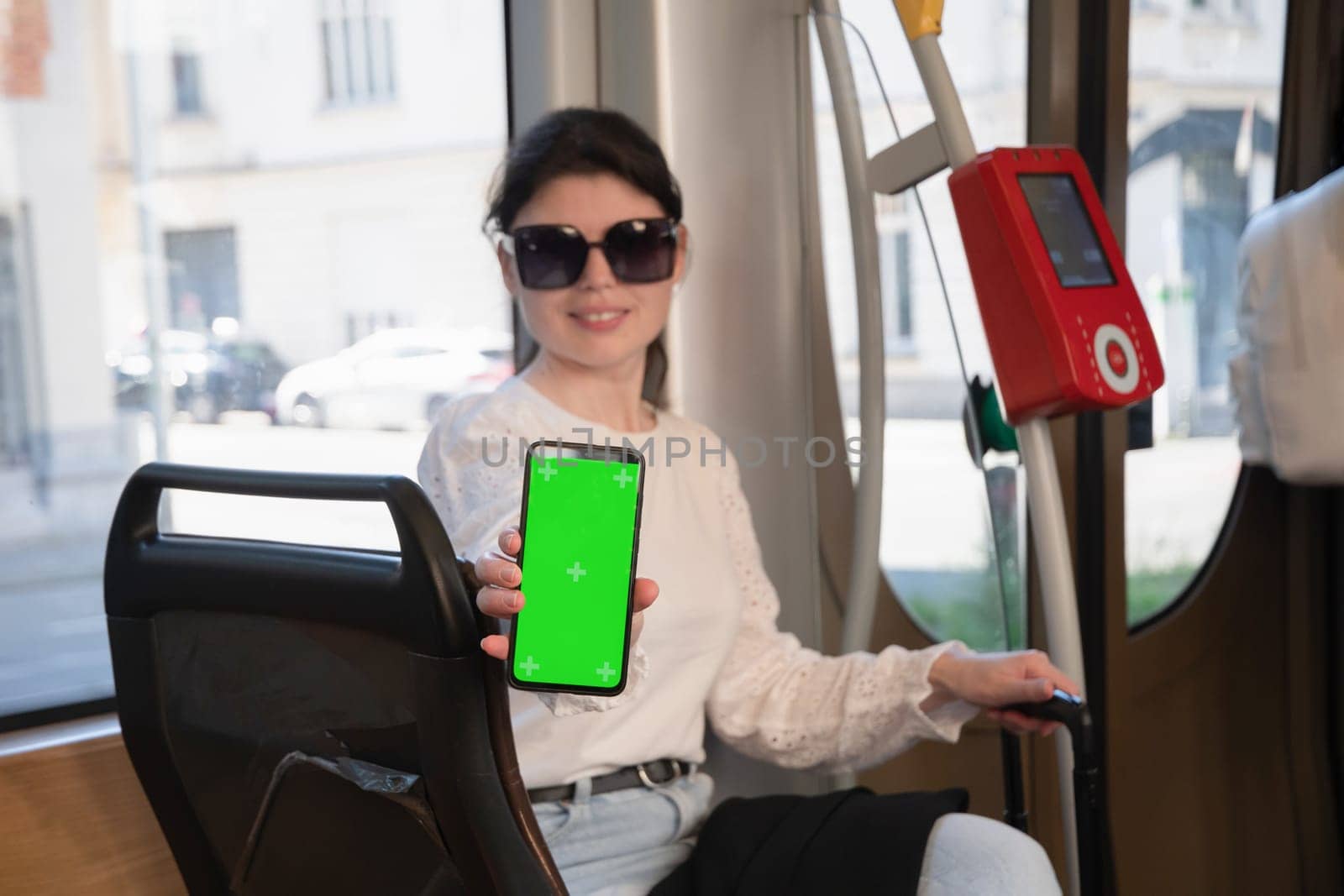 brunette woman showing smartphone with vertical green screen in tram, next to the digital checkout High quality photo