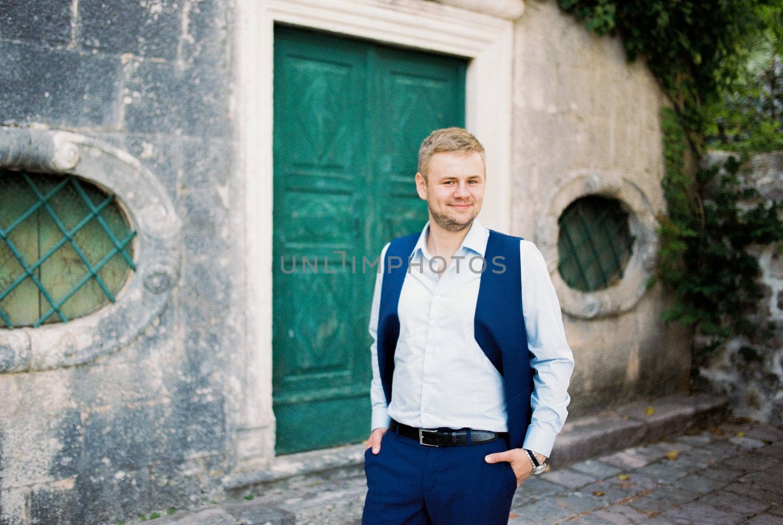 Young man in a vest with his hands in his pockets stands near an old building in the park. High quality photo