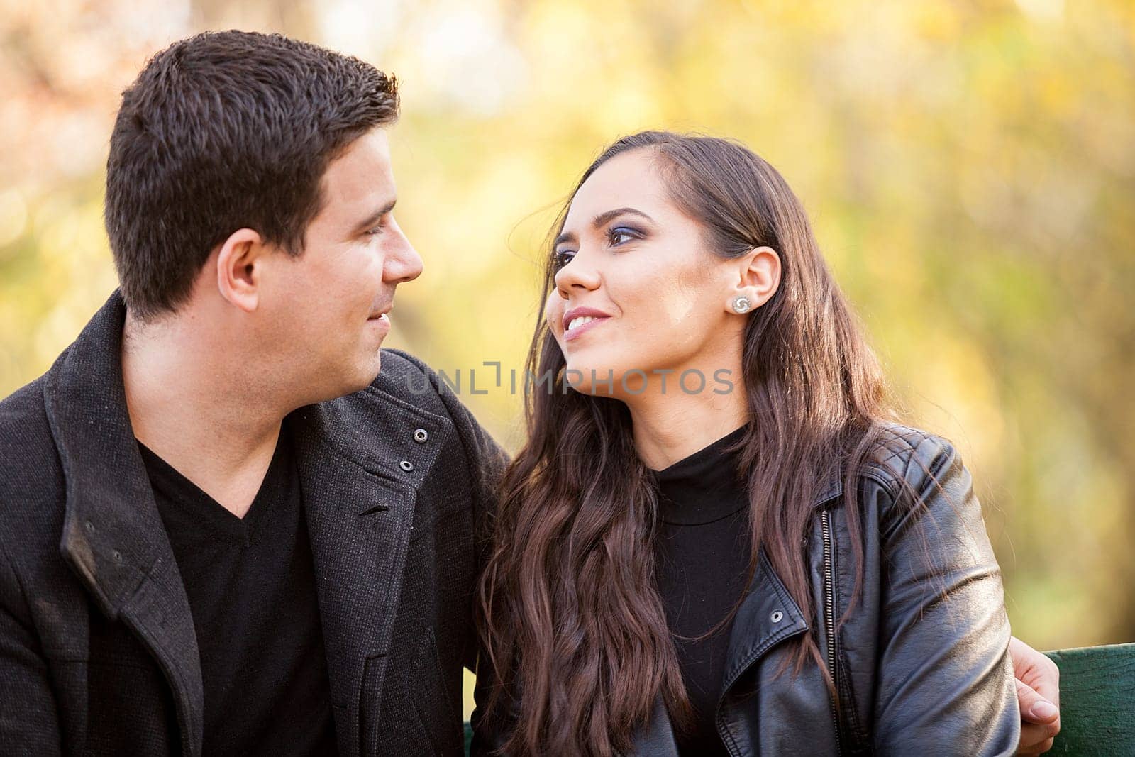 Close up of beautiful in love couple sitting on a bench in autumn park