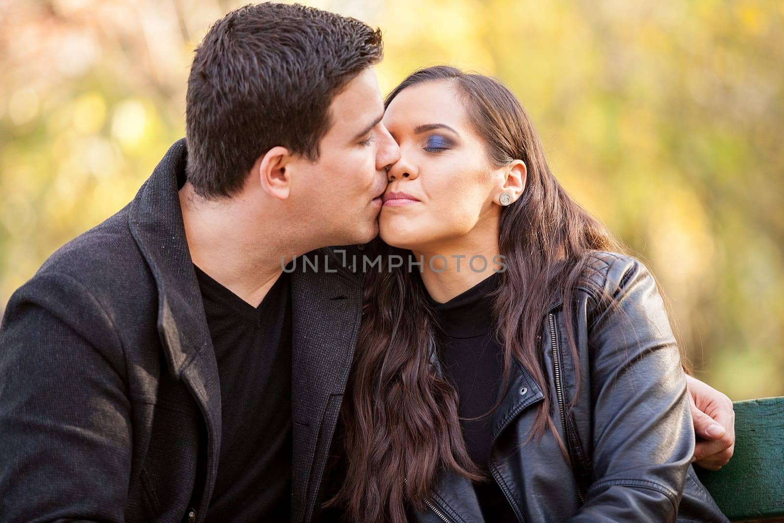 Close up of beautiful in love couple sitting on a bench in autumn park