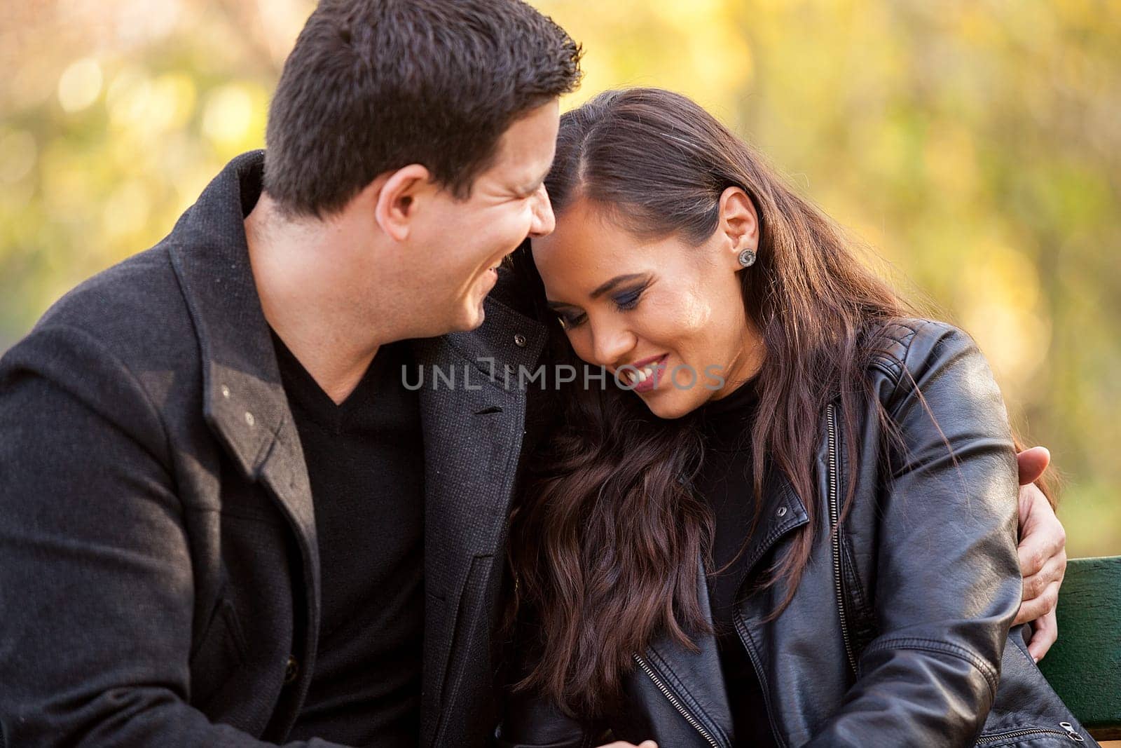 Close up of happy beautiful in love couple sitting on a bench in autumn park