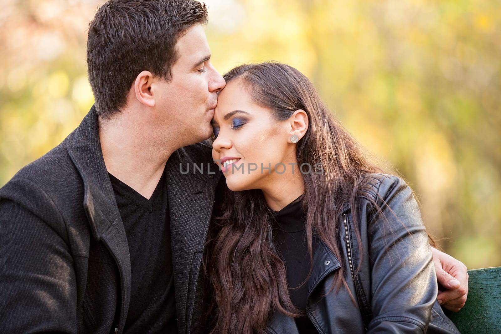 Close up of beautiful in love couple sitting on a bench in autumn park