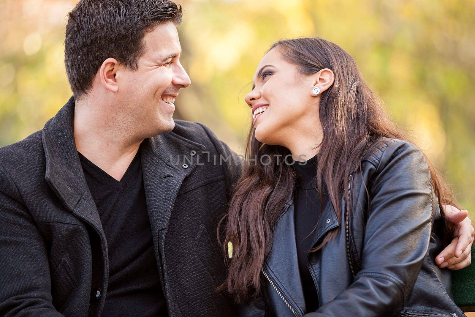 Close up of happy beautiful in love couple sitting on a bench in autumn park