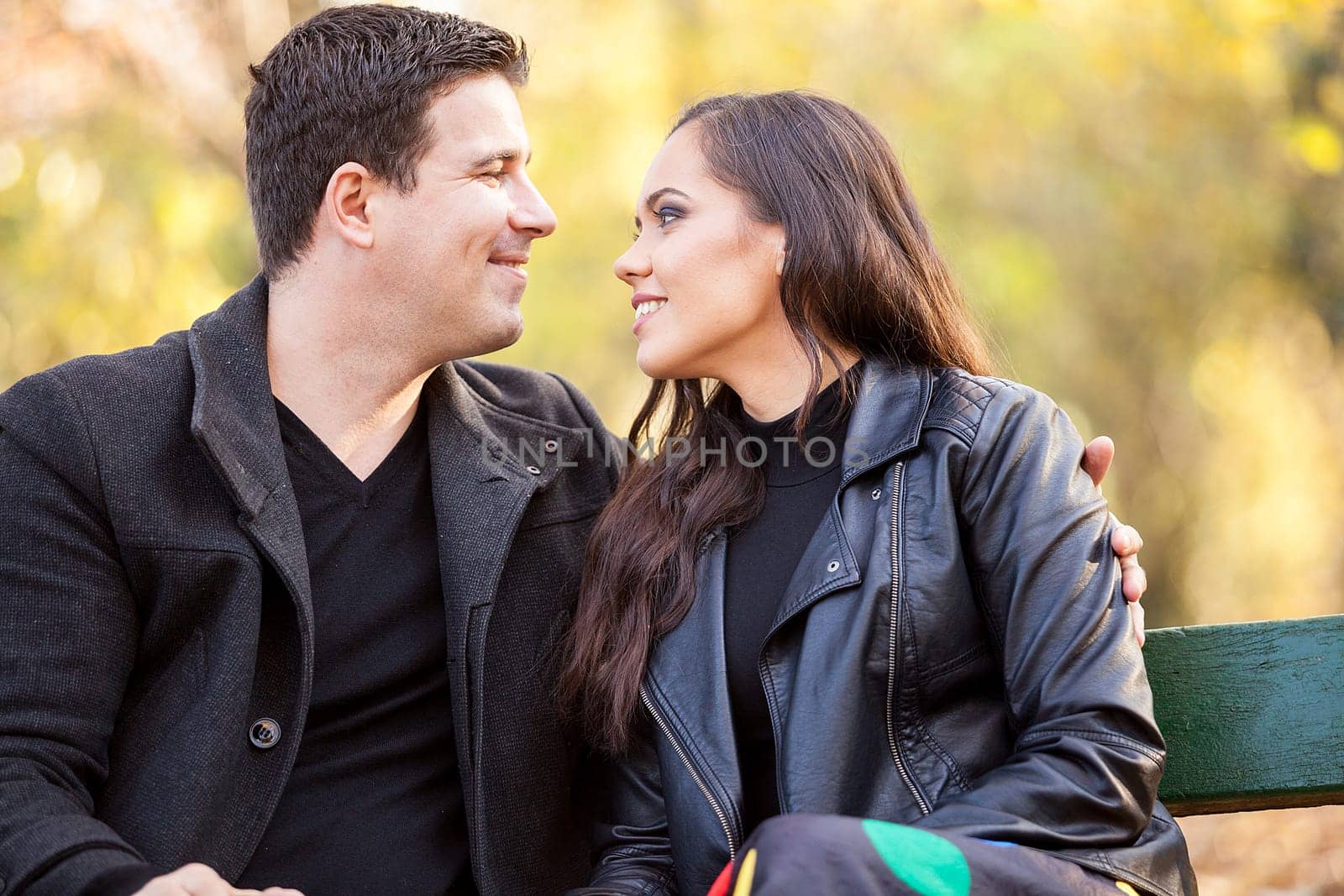 Close up of smiling in love couple sitting on a bench in autumn park