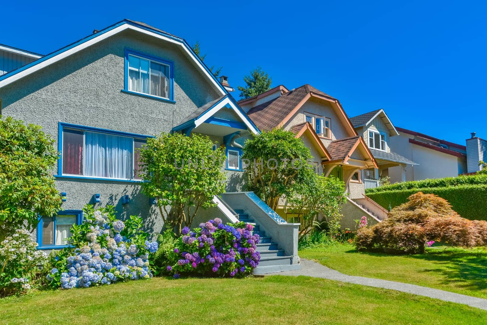 Snug warm family houses side by side. Residential house with the pathway over front yard lawn on blue sky background.