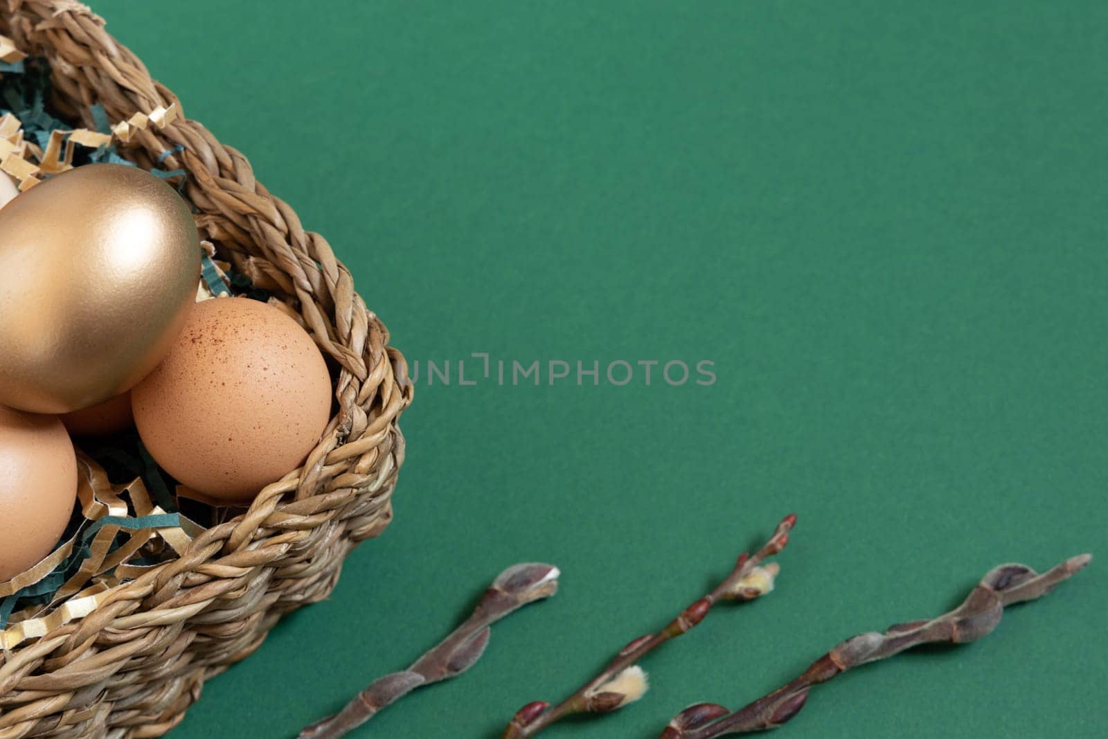 Easter eggs natural and gold in basket with paper filler . Branch of willow catkins. Light pastel orange background with copy space.