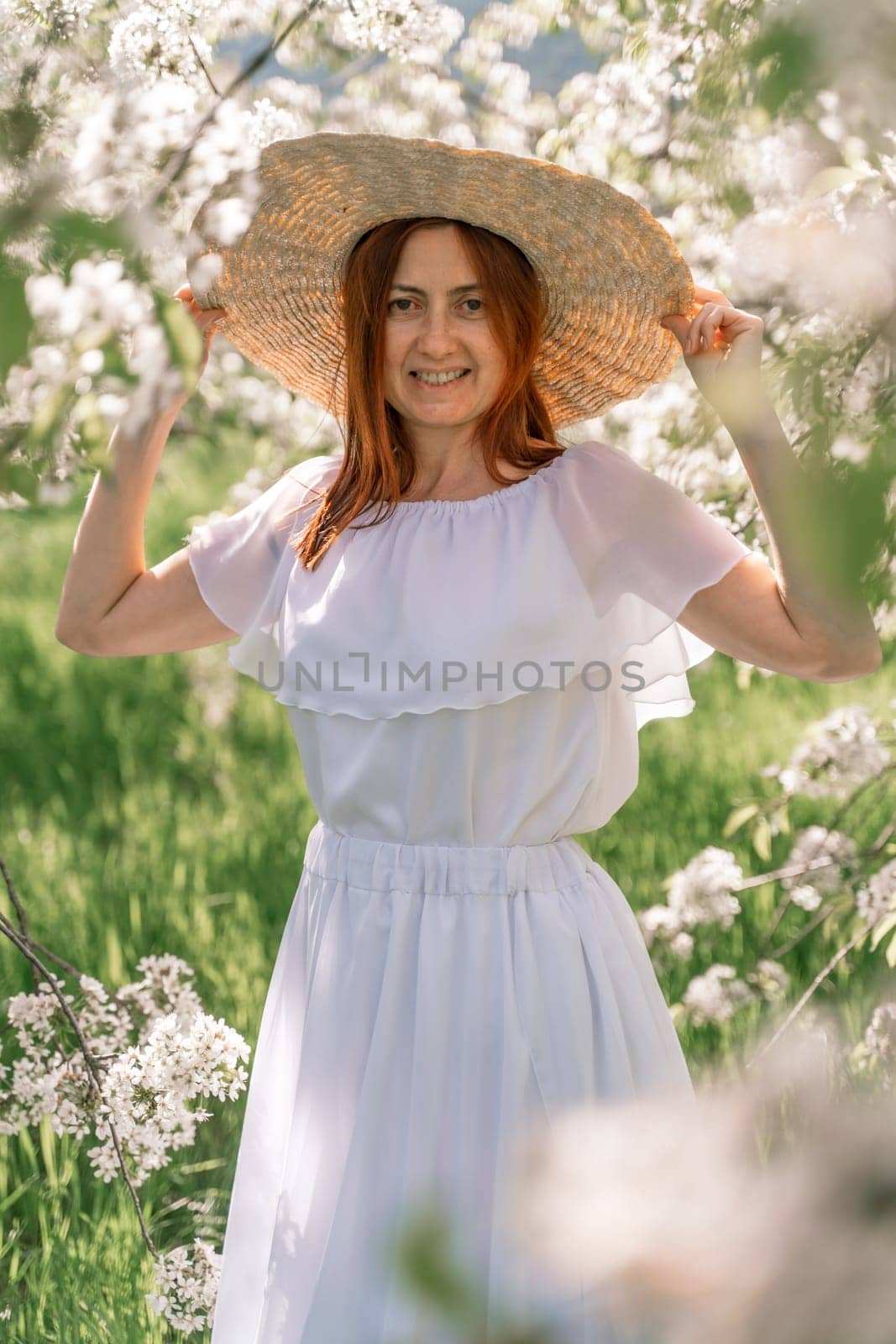 Woman cherry orchard. A happy woman in a long white long dress walks through the green spring blooming cherry garden. Happy cheerful princess bride. The fabric of the skirt flutters in the wind. by Matiunina