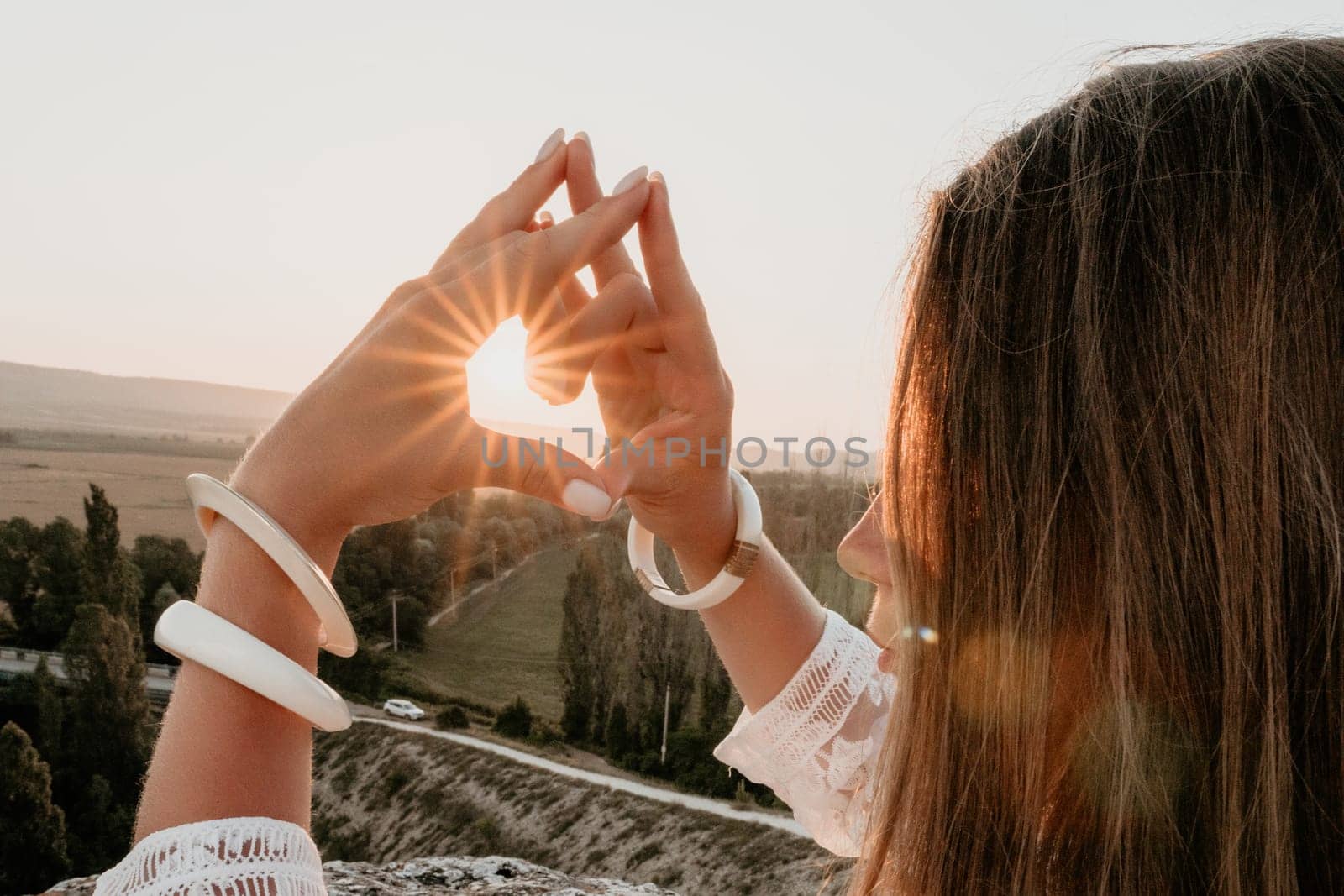 Romantic beautiful bride in white dress posing with sea and mountains in background. Stylish bride standing back on beautiful landscape of sea and mountains on sunset