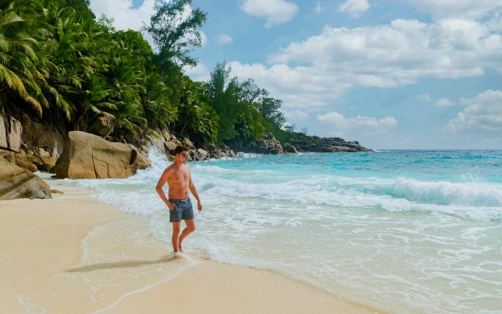 Young men in a swim short on a white tropical beach with palm trees Petite Anse beach Mahe Tropical Seychelles Islands.