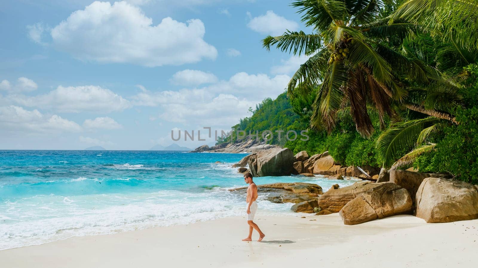 Young men in a swim short on a white tropical beach with palm trees Petite Anse beach Mahe Tropical Seychelles Islands.
