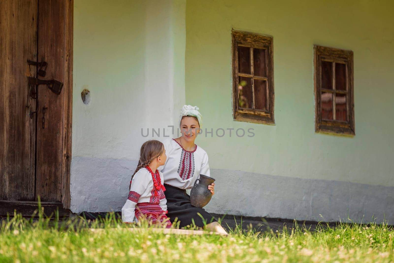 mother and daughter in traditional Ukrainian clothes are sitting near the house