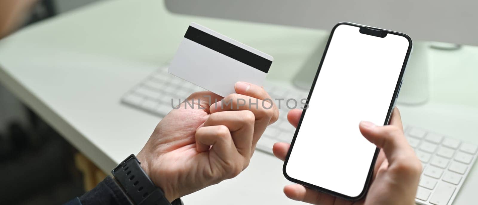 Close up view of man holding credit cad and using mobile phone smartphone for online banking transaction.