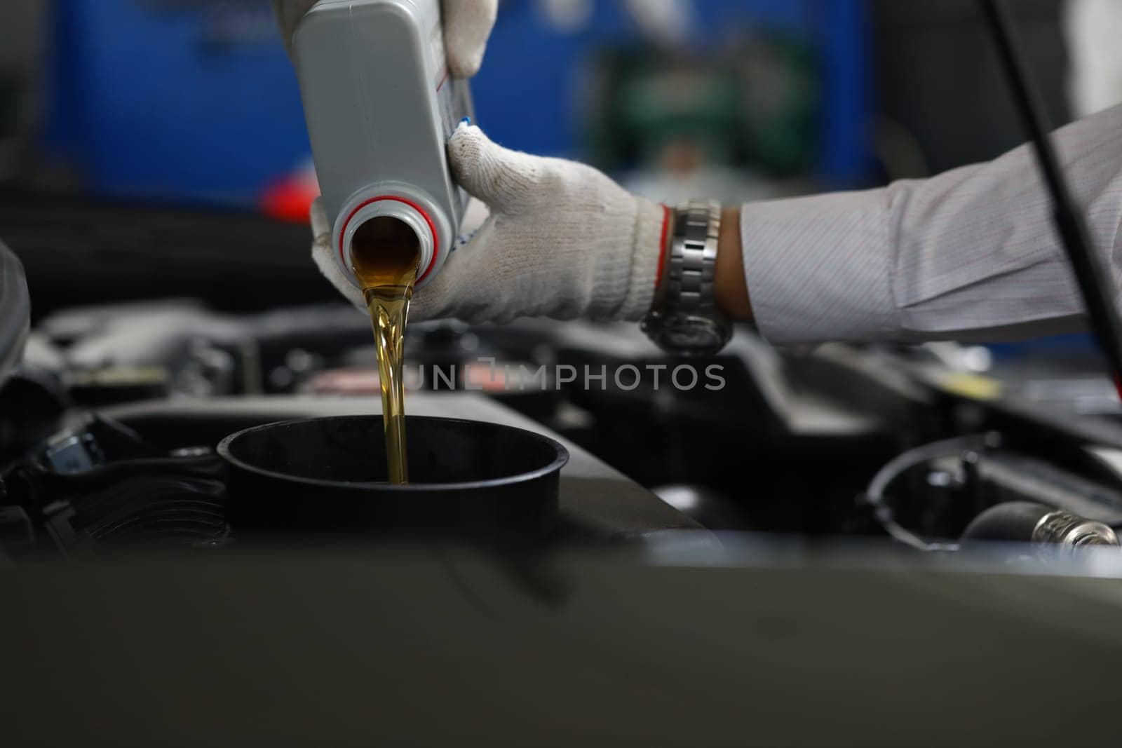 Car mechanic pours engine oil into car engine closeup. Oil change auto concept