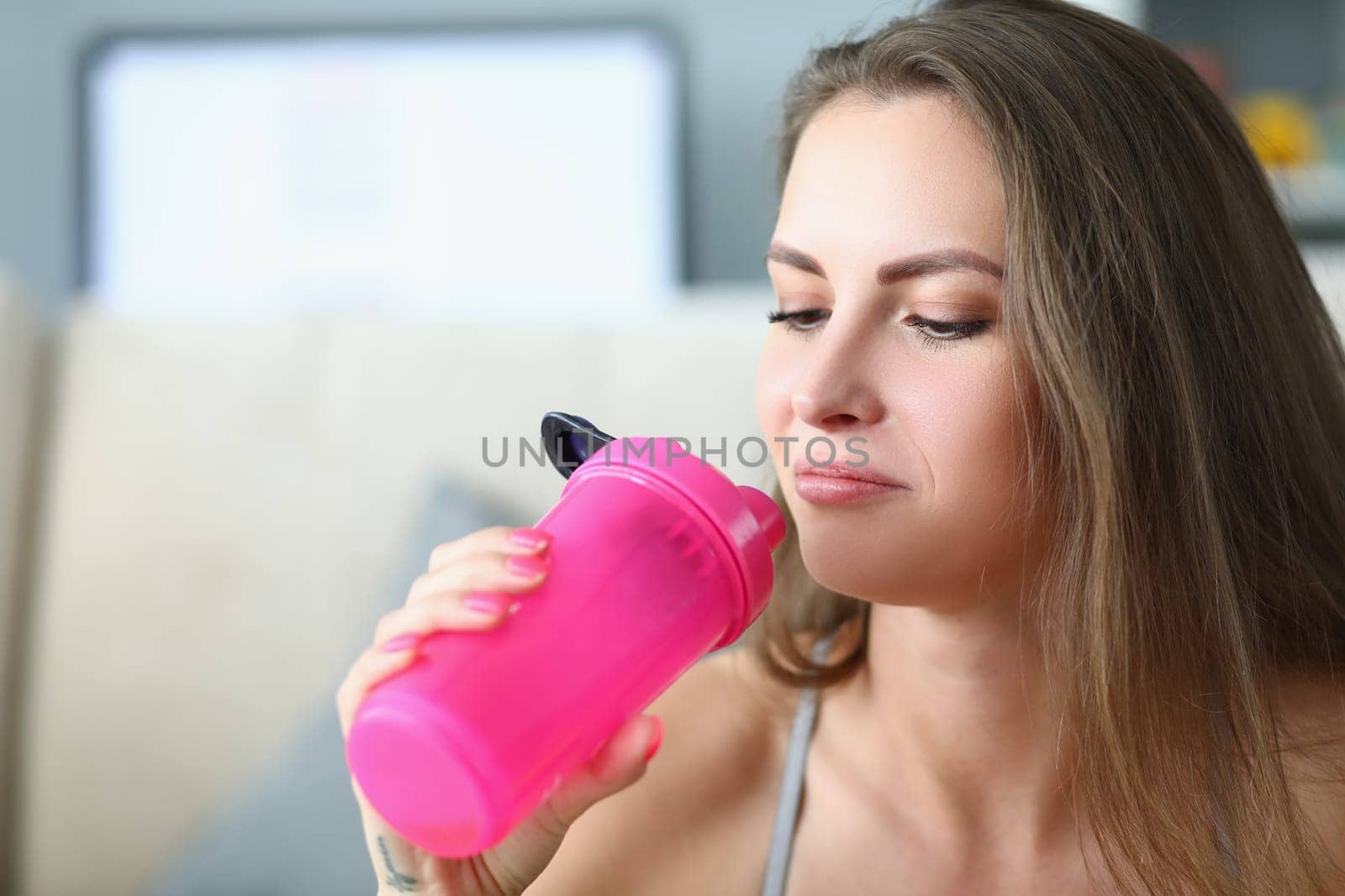 Portrait of young calm pensive woman with bottle of water. Sports training and drinking regimen concept