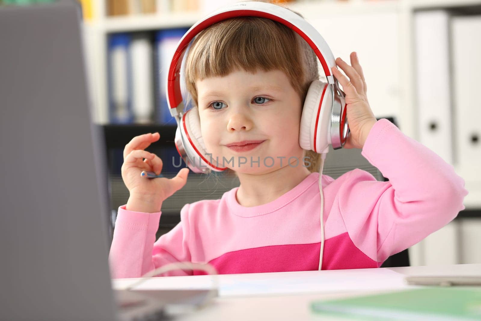 Portrait of cute girl in headphones watching cartoons using laptop computer. Distance learning and home education for children