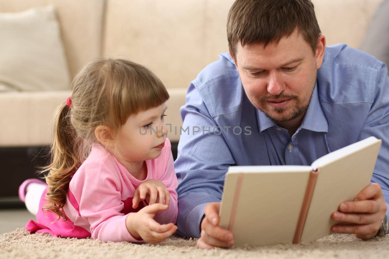 Father is reading book to daughter lying on floor in bedroom. Family reading and sharing time concept