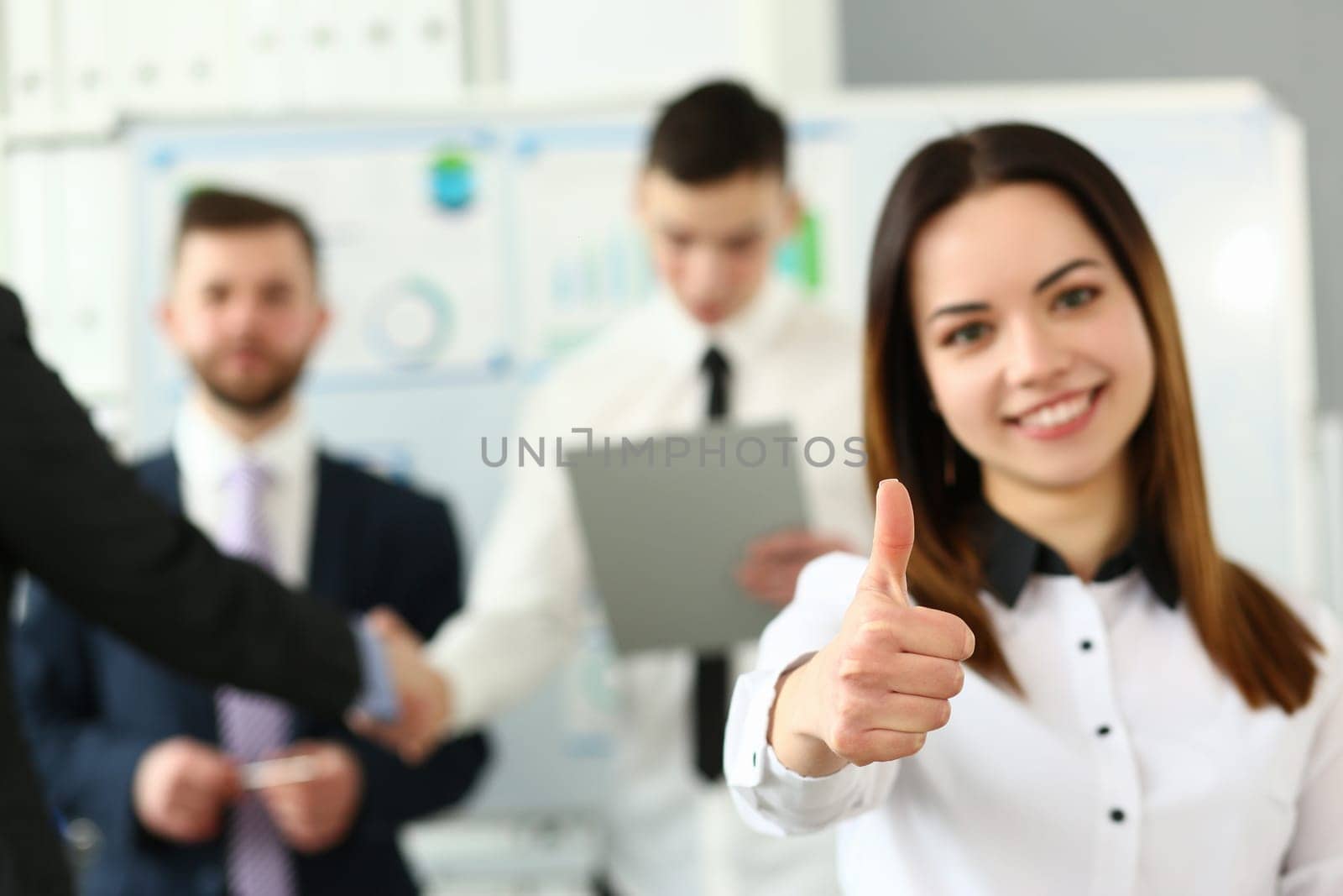 Businesswoman feels confident in team and thumbs up gesture. Happy businesswoman showing thumbs up and smiling colleagues standing in background