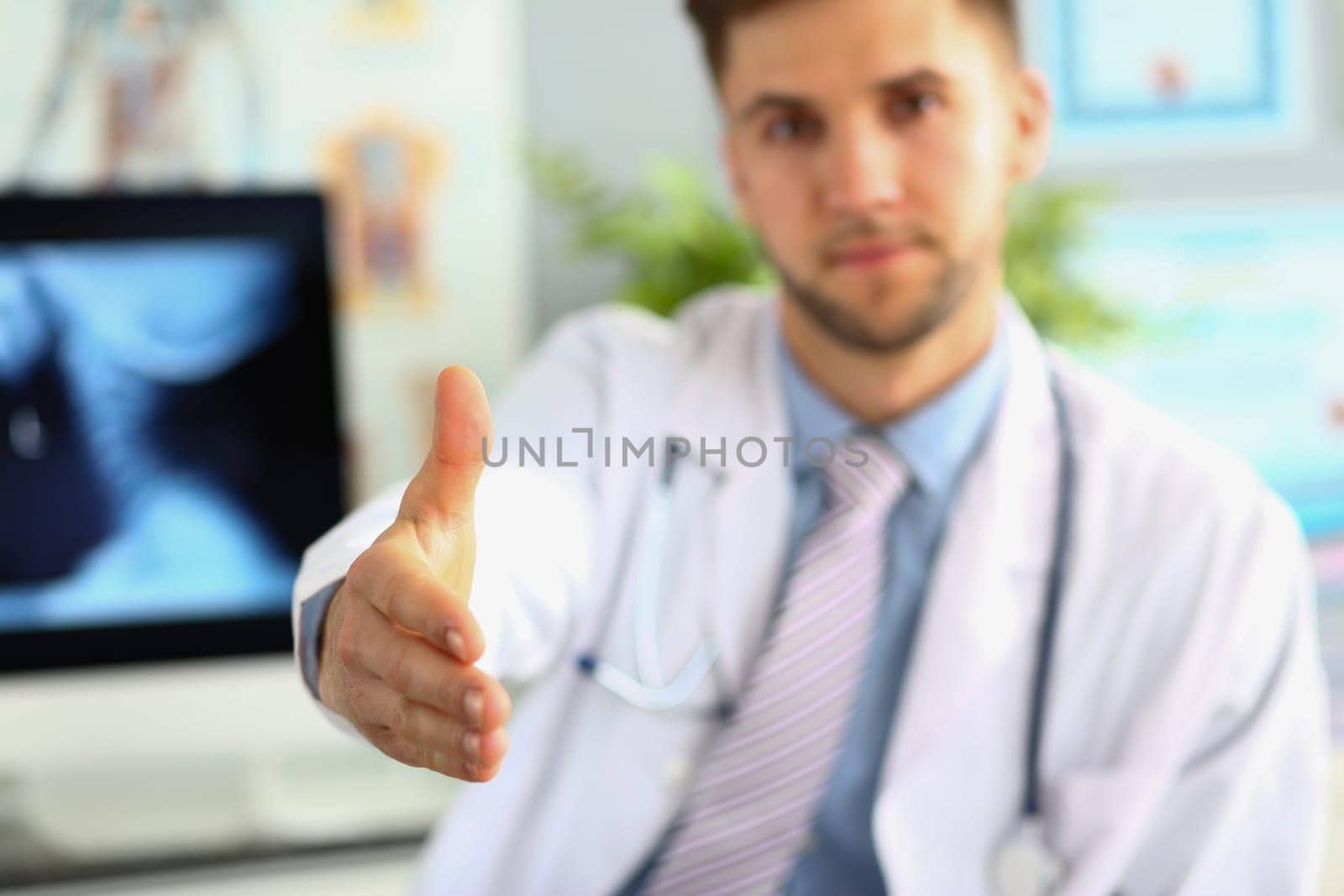 Closeup of male doctor offering handshake in office. Welcome gesture and health insurance concept