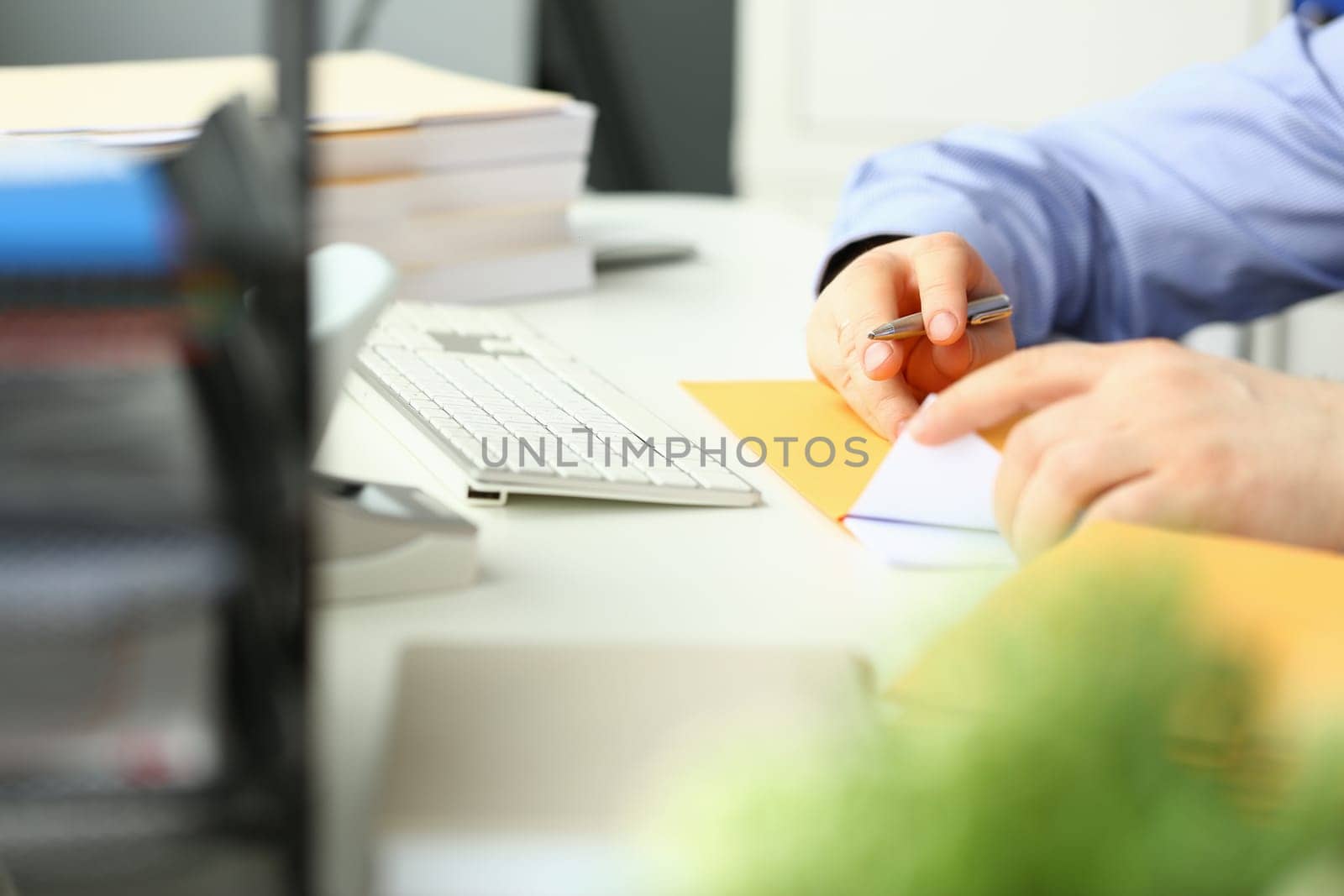 Businessman is sitting at table in office holding yellow envelope and taking out sheet of notification of a received paper letter closeup. Business correspondence corporate news and notice