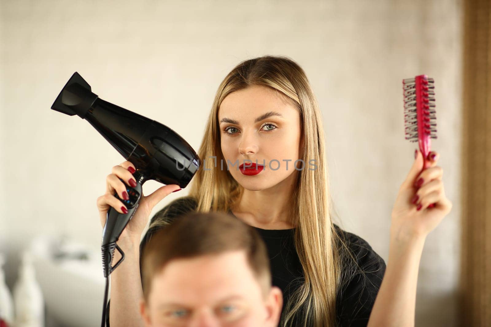 Woman hairdresser is holding hair dryer and hairbrush man is sitting in barbershop chair. Stylish trendy men's hairstyles and styling concept